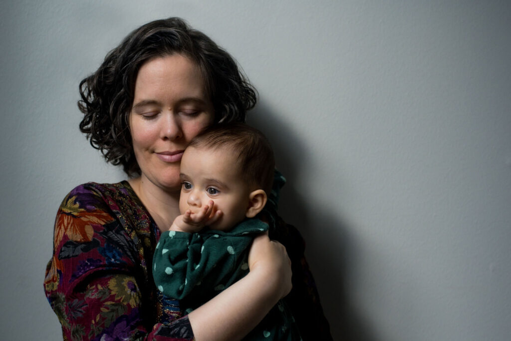 a mother poses with her newborn baby against a gray wall
