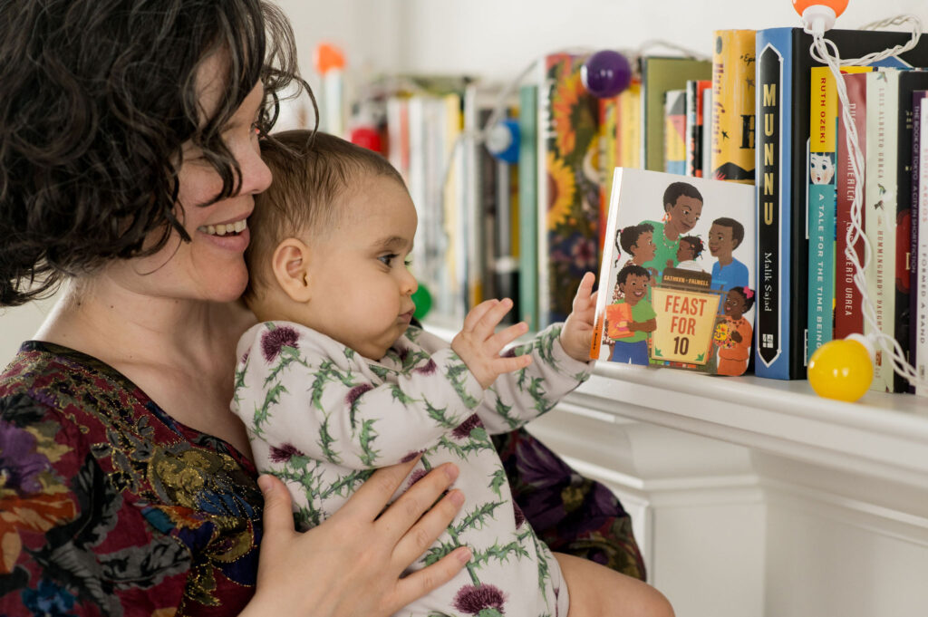 A mother poses with her newborn baby in their nursery with some books