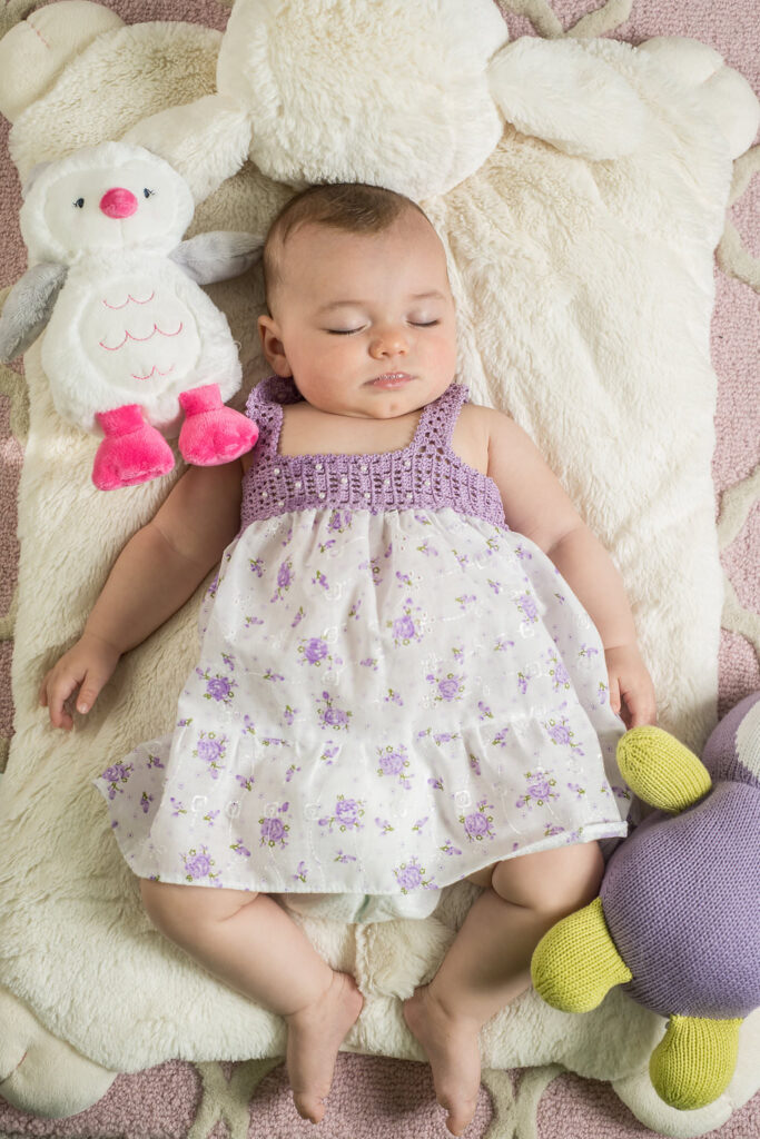 a newborn girl wearing a purple and white dress sleeps in her crib