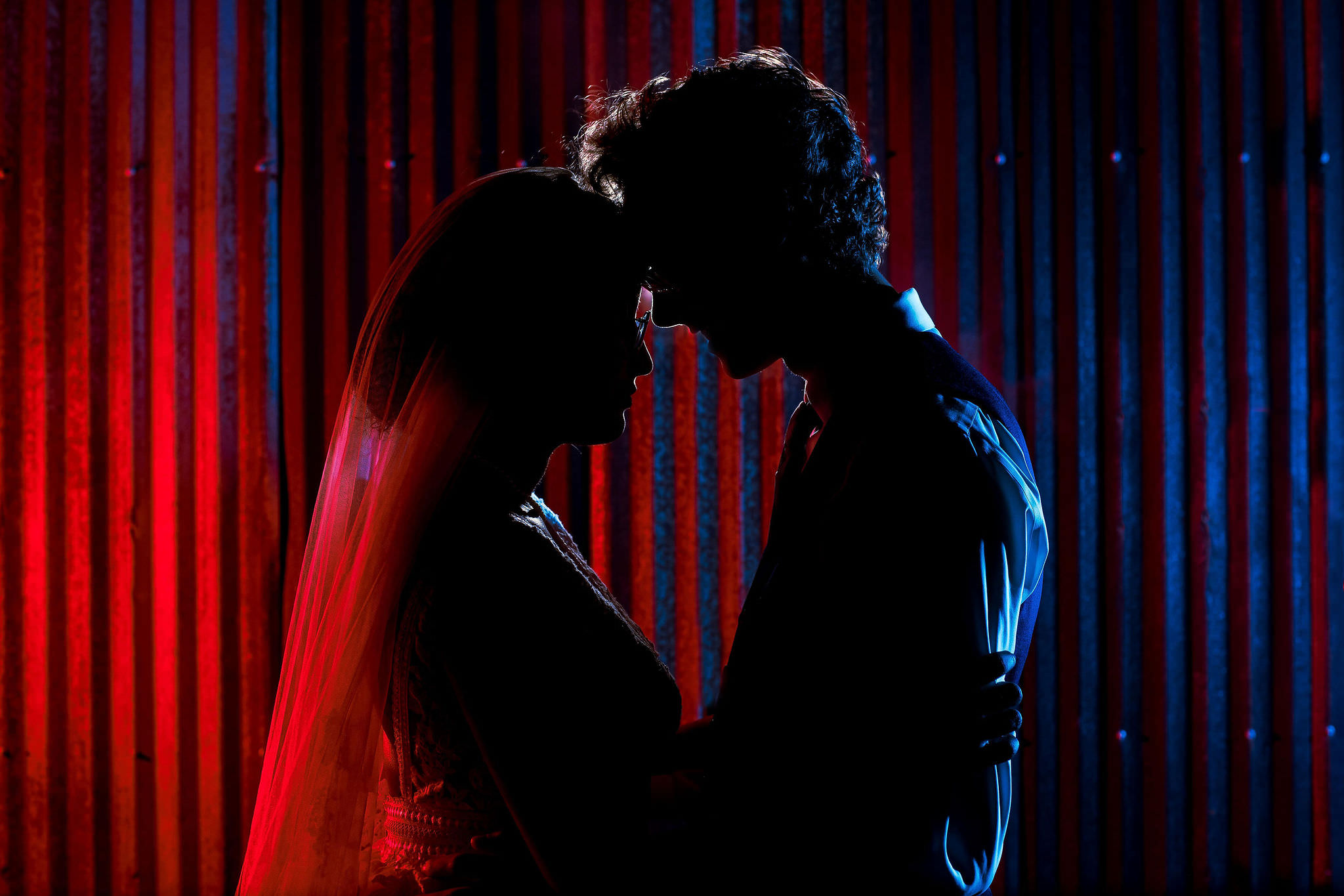 a couple poses for their wedding photos. One is lit by a blue light and the other is lit with a red light