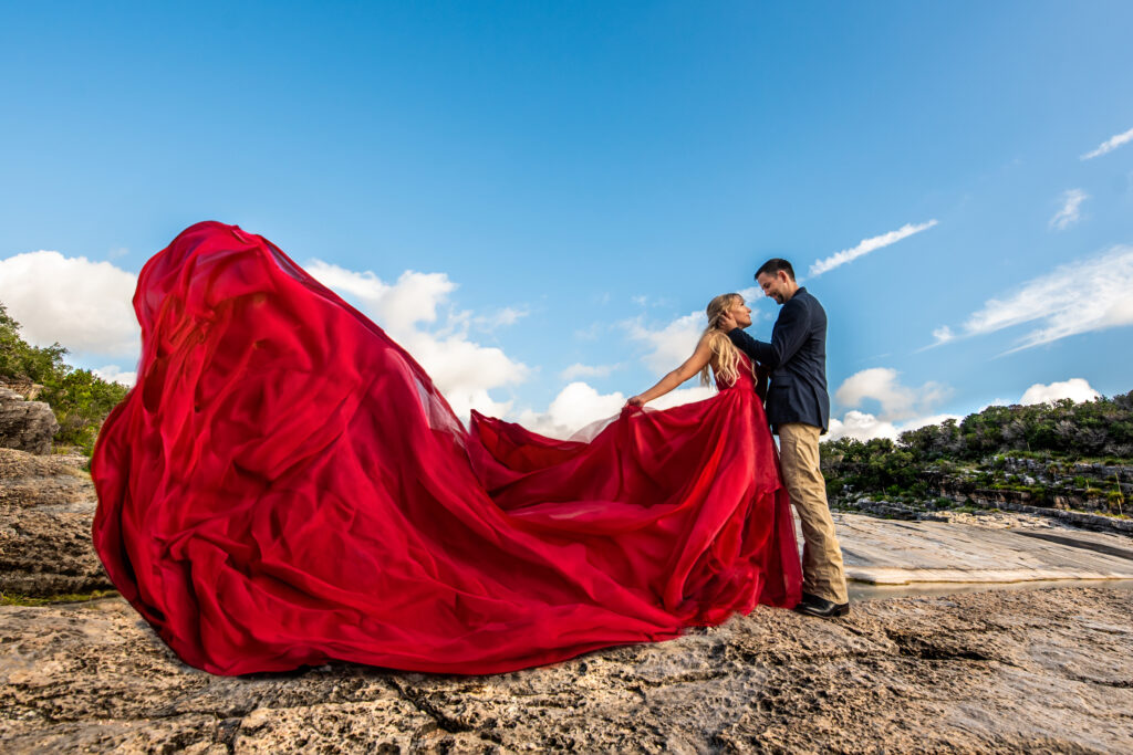 A couple's engagement photo, woman wears a dramatic flowing red dress while looking at fiance