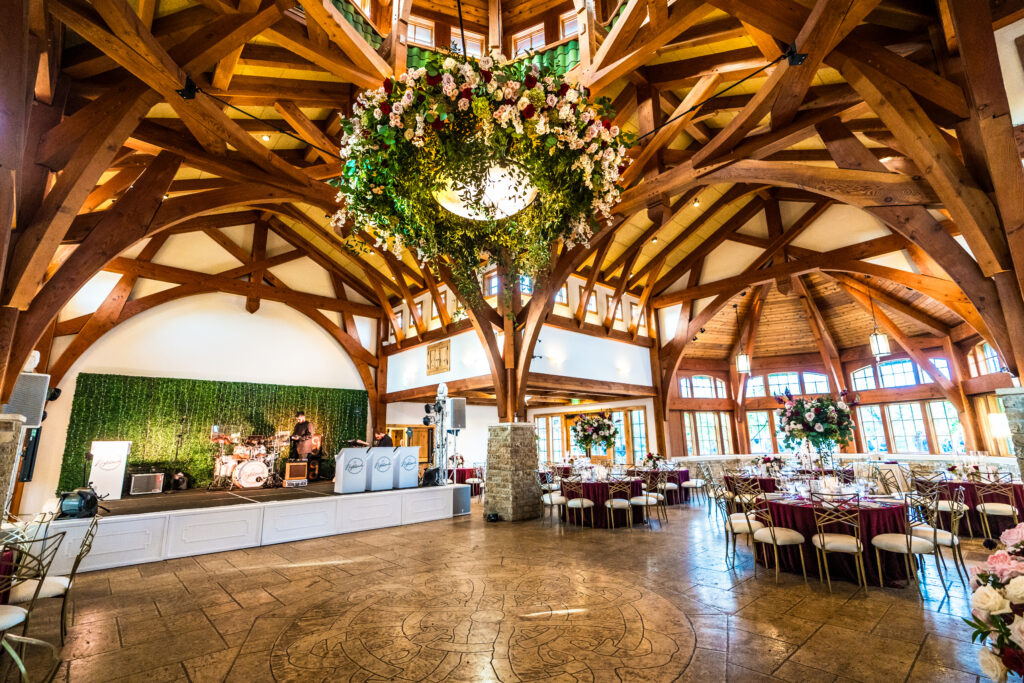 Elegant wedding reception hall at Sacred Oaks, Camp Lucy with wooden beams, floral chandelier, and a stage setup.